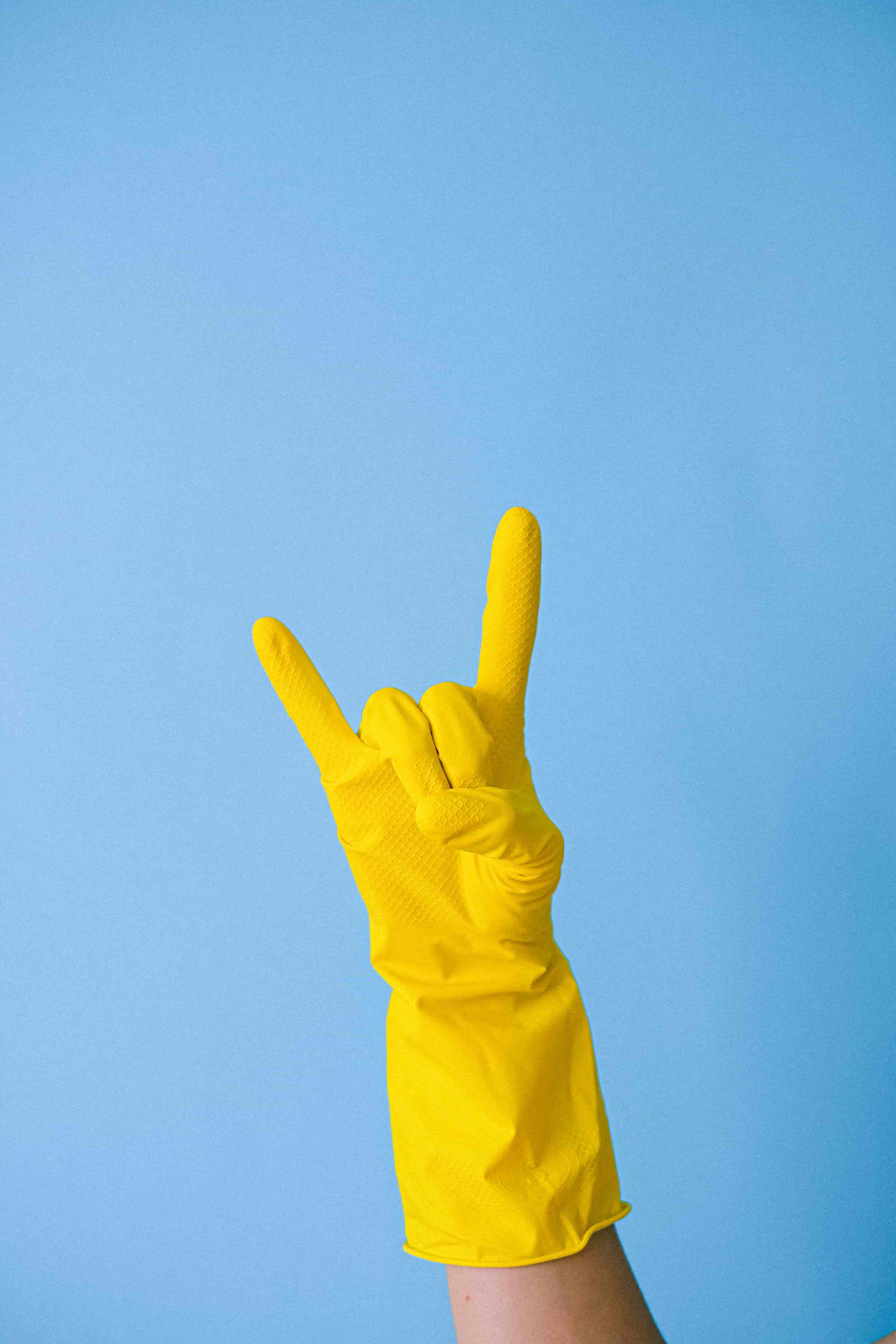 A hand wearing a yellow cleaning glove formed into the Rock I love you sign